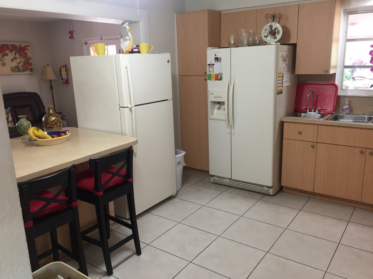 A kitchen with two refrigerators and a counter with chairs.