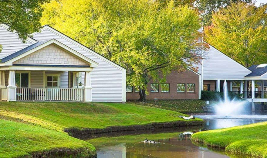 A picturesque view of a house by a pond surrounded by lush greenery.
