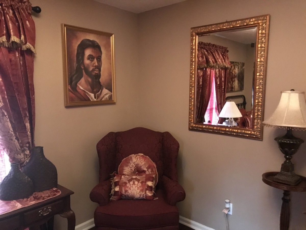 A cozy corner of a living room featuring an armchair, a painting on the wall, a decorative mirror, and a lamp.