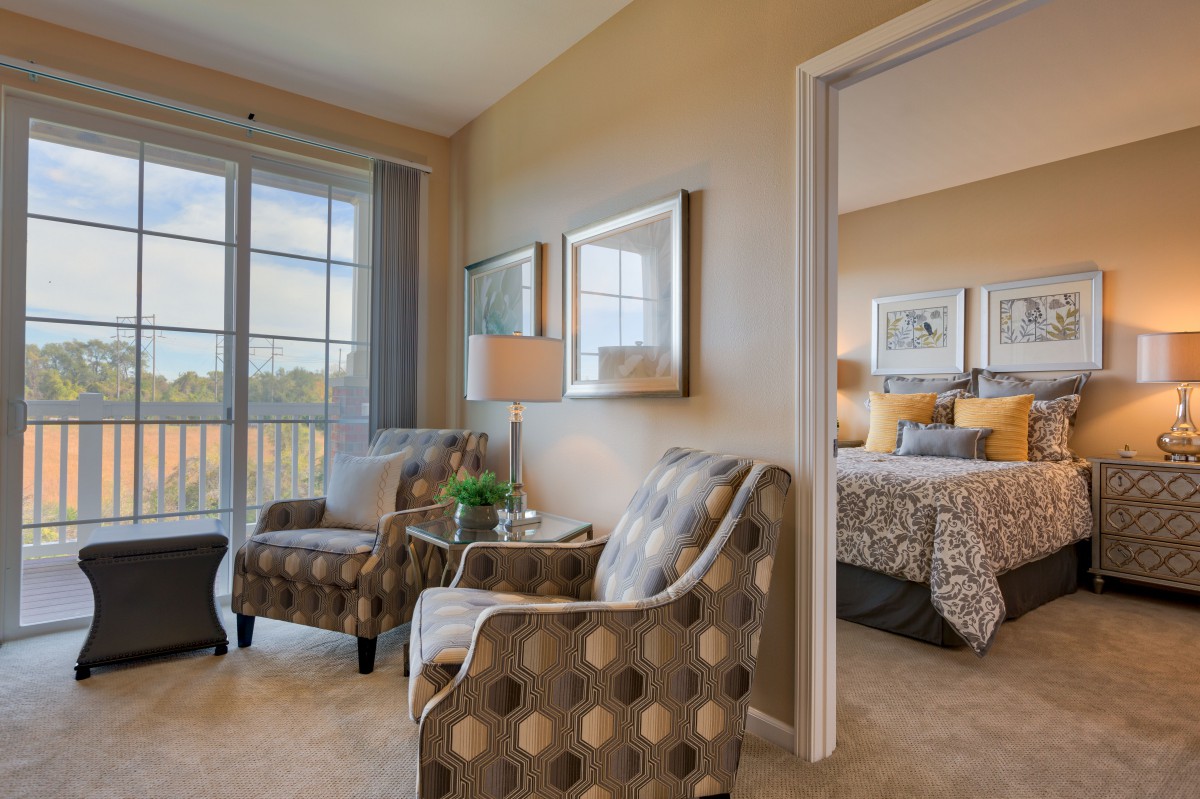 A cozy living space with patterned chairs and a view into an inviting bedroom.