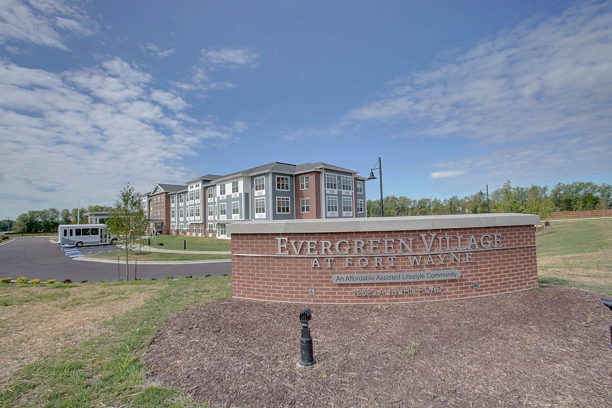 A modern apartment complex with a brick entrance sign under a partly cloudy sky.