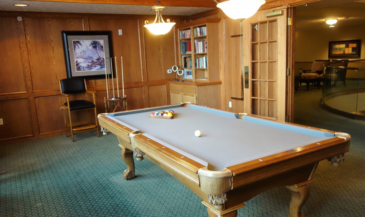 A well-furnished game room featuring a pool table, warm wood paneling, and comfortable lighting.