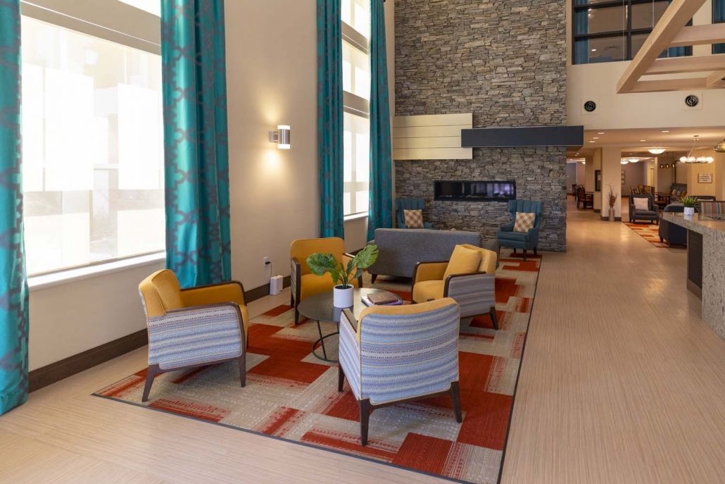 A modern living area with colorful chairs and a stone fireplace, featuring bright teal curtains and a vibrant rug.