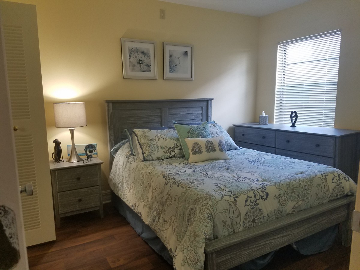 A cozy bedroom with a neatly made bed, bedside lamp, dresser, and window.