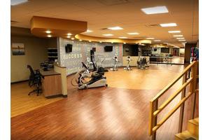 A spacious gym with various exercise equipment and a wooden floor.