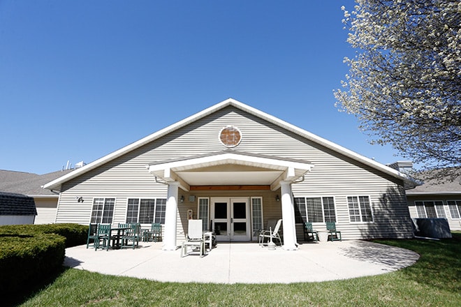 A single-story building with a gabled roof and a welcoming entrance surrounded by outdoor seating, set against a clear blue sky.