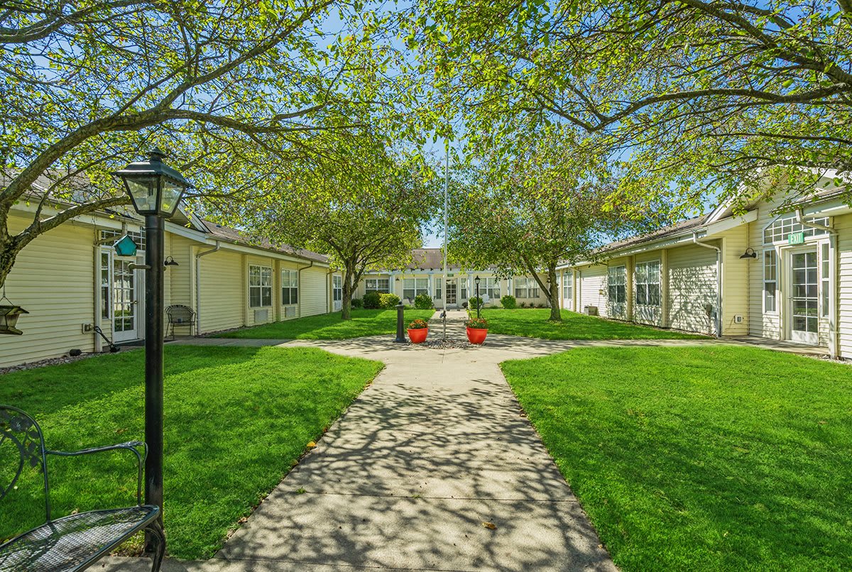 A tranquil courtyard with a central pathway, surrounded by lush greenery and buildings.