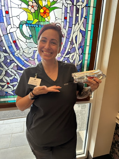 A healthcare worker smiling while proudly holding an item near a beautiful stained glass window.
