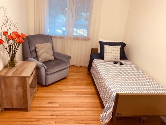 A cozy bedroom with a single bed and an armchair, featuring hardwood flooring and minimalist decor.