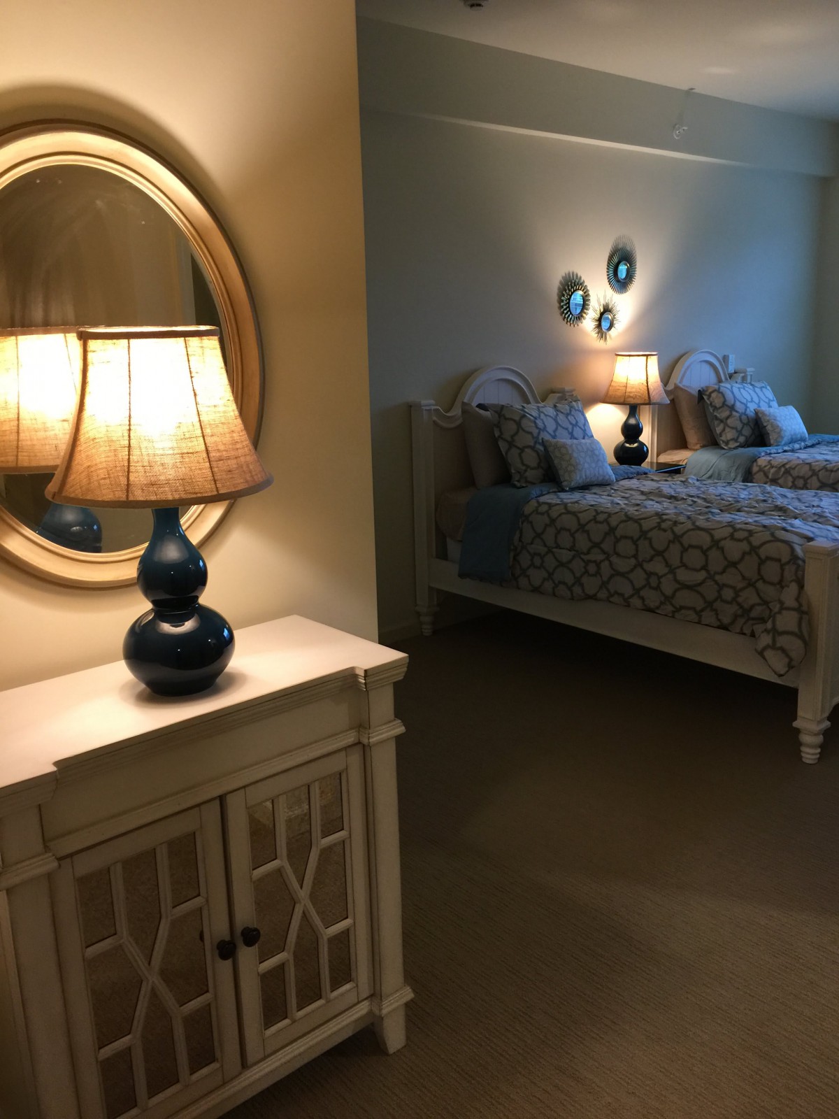 A cozy bedroom featuring a softly lit lamp, twin beds, and a decorative mirror.