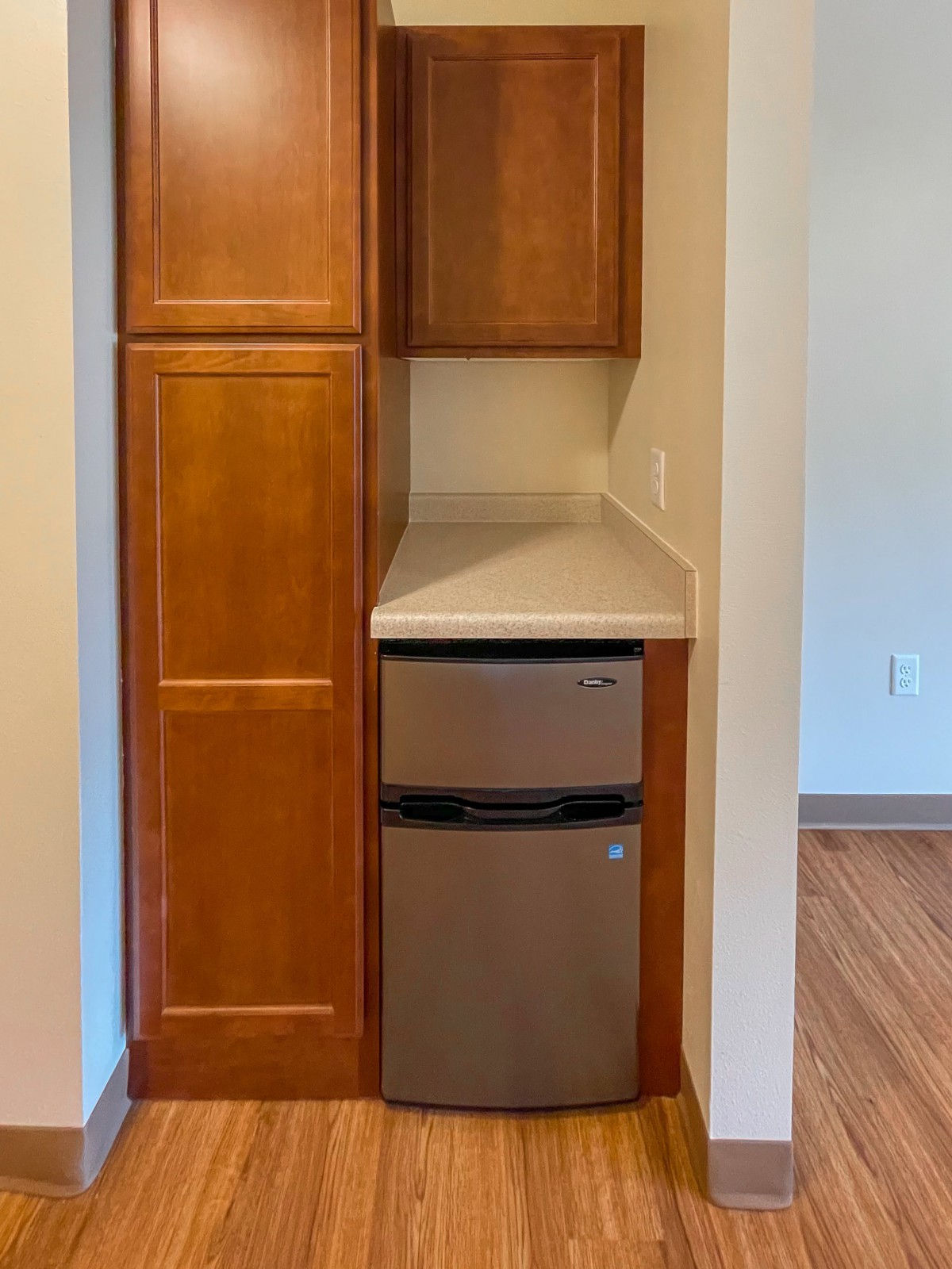A small kitchen area featuring wooden cabinets, a mini fridge, and a countertop.
