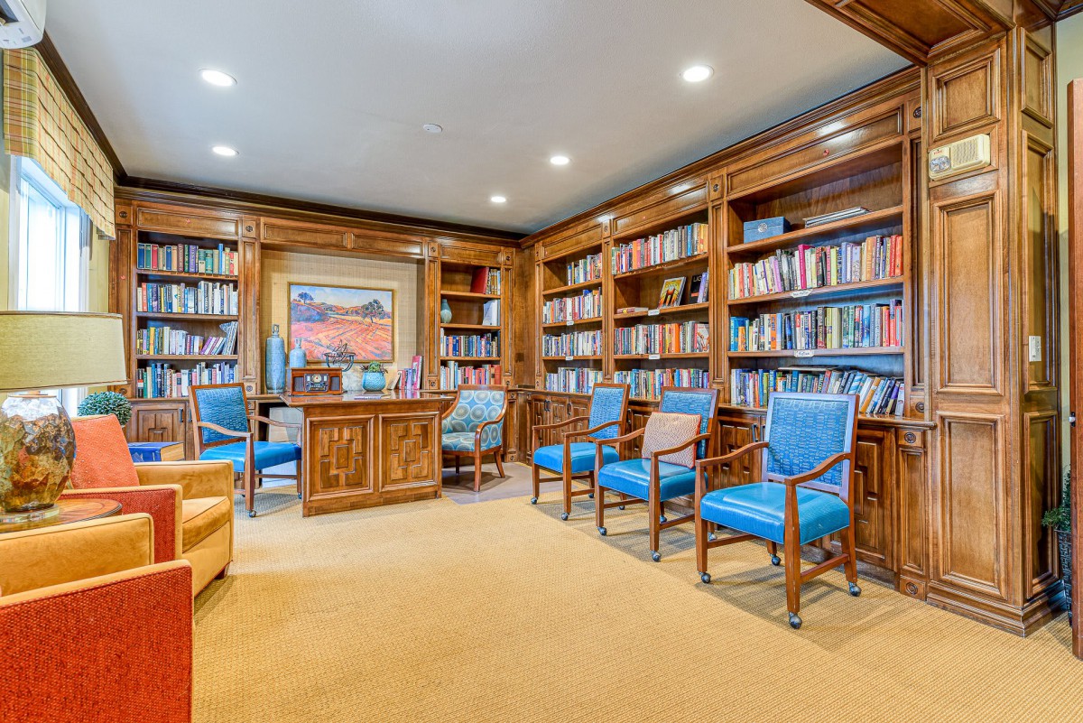 A cozy library room filled with books and wooden furniture, featuring artwork on the wall.