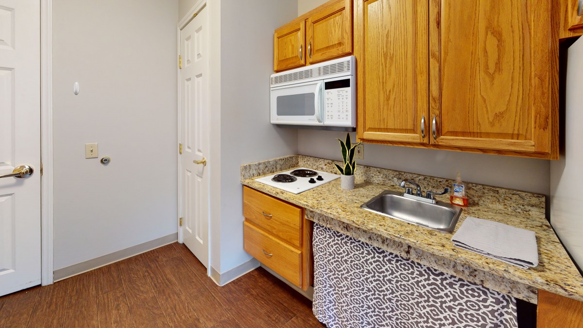 A compact kitchen with wooden cabinets, a granite countertop, a built-in microwave, and a small stovetop.