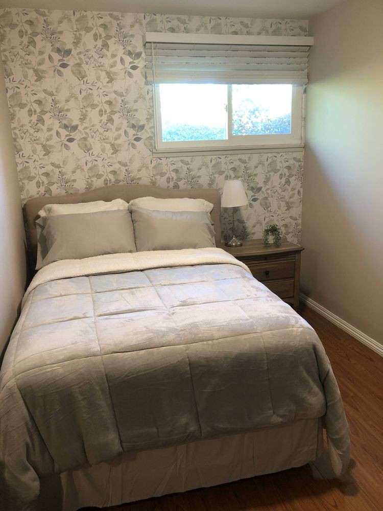 A cozy bedroom with a neatly made bed and floral wallpaper.