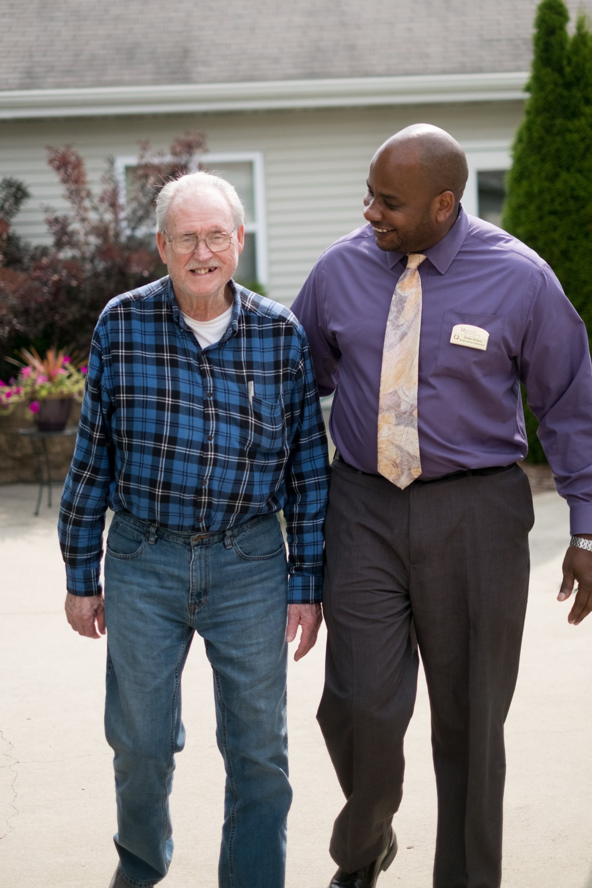 A caregiver assists an elderly man while walking outdoors.