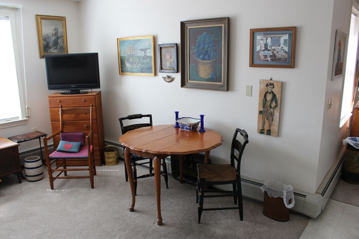 A cozy living room with a round dining table, surrounded by chairs and decorated with various artworks on the walls.