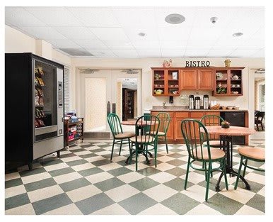 A cozy kitchen area with tables, chairs, a vending machine, and wooden cabinets.