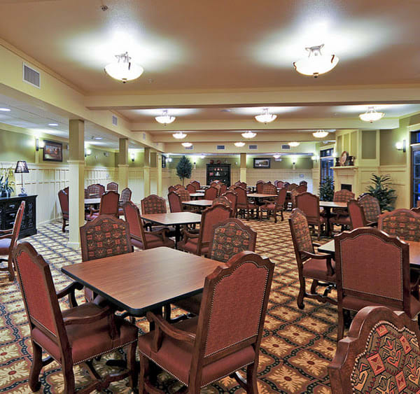 A spacious dining area with elegantly arranged tables and chairs, illuminated by ceiling lights.