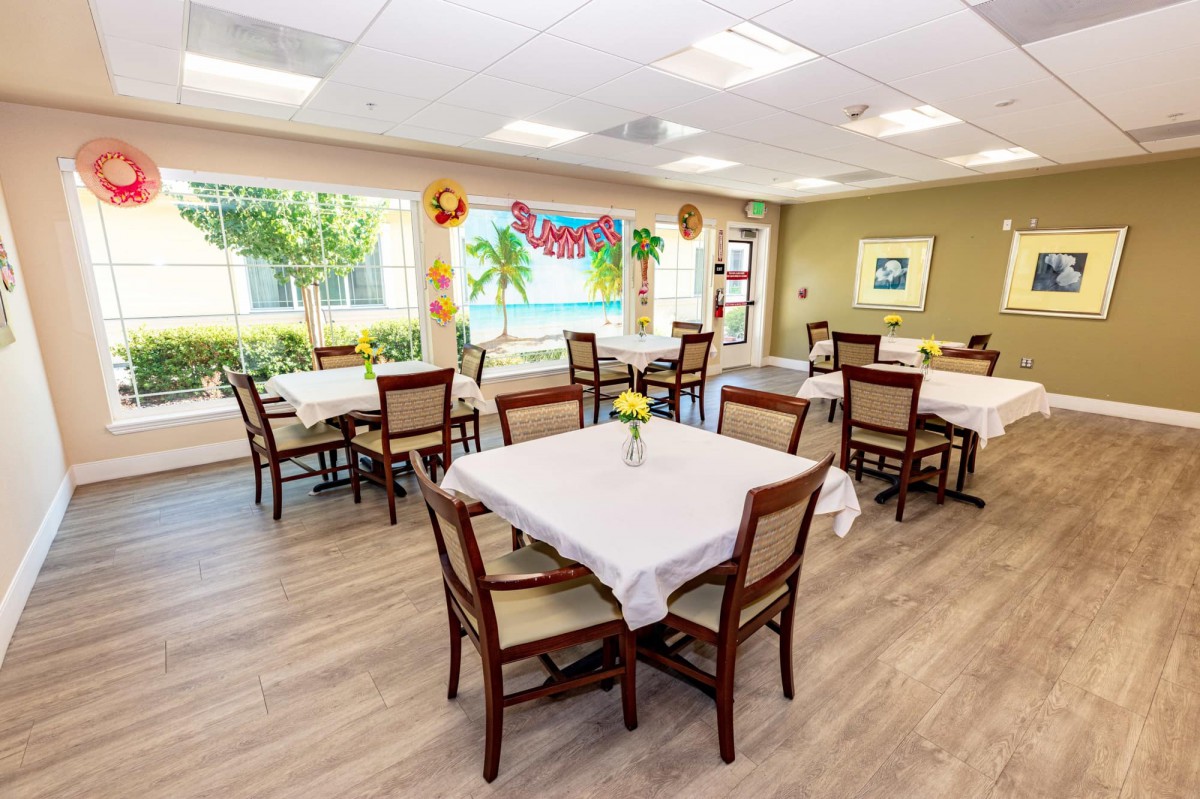 A well-lit dining room with tables and chairs, featuring colorful decorations and large windows.