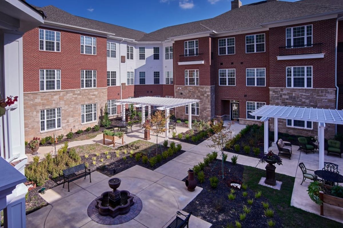 A peaceful courtyard with a fountain and seating area surrounded by a brick residential building.