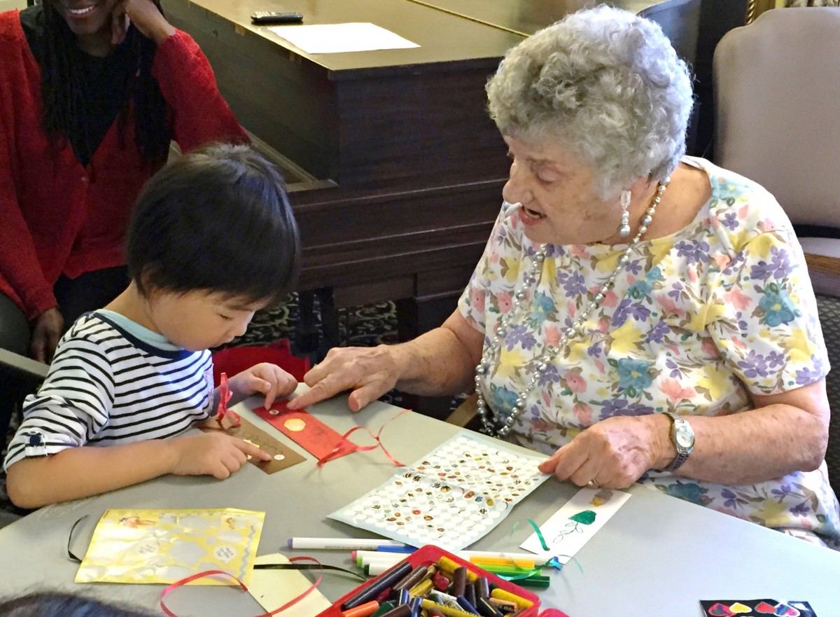 An elderly woman and a young child engage in a crafting activity together, surrounded by art supplies.
