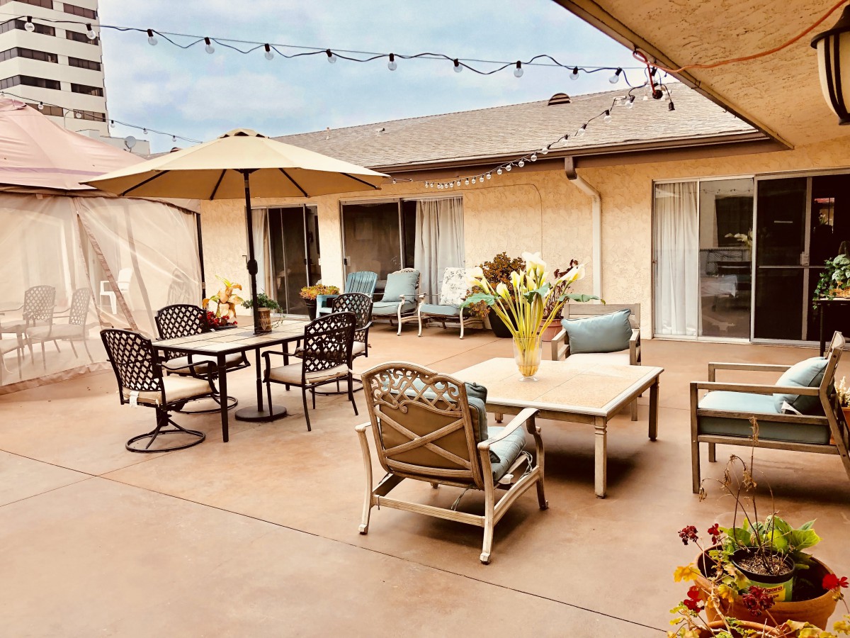 A cozy outdoor patio area featuring tables, chairs, umbrellas, and decorative plants under string lights.