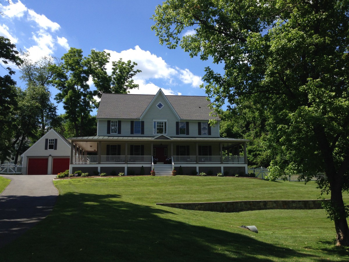 A charming suburban house with a spacious lawn and a wrap-around porch.