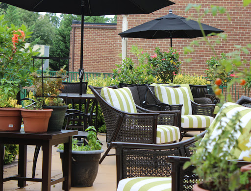 A cozy outdoor seating area featuring stylish wicker chairs with striped cushions, surrounded by greenery and shaded by black umbrellas.