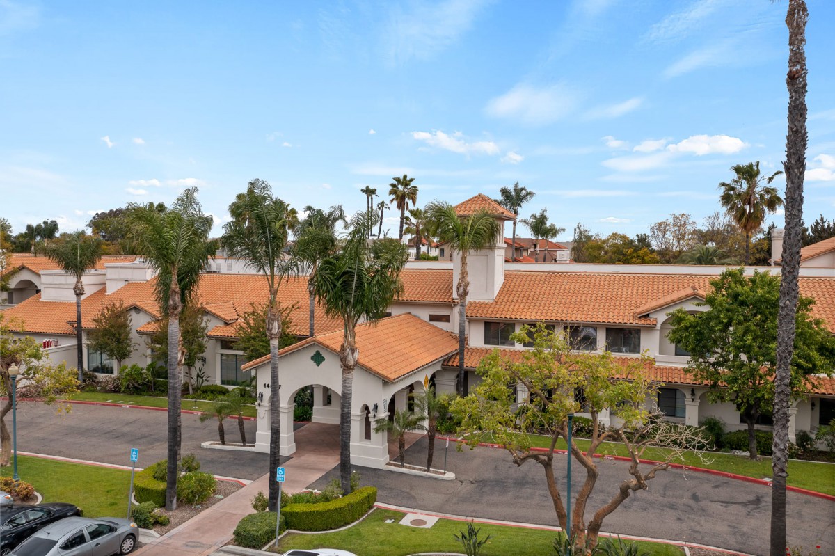 Aerial view of a building with orange-tiled roofs surrounded by palm trees.