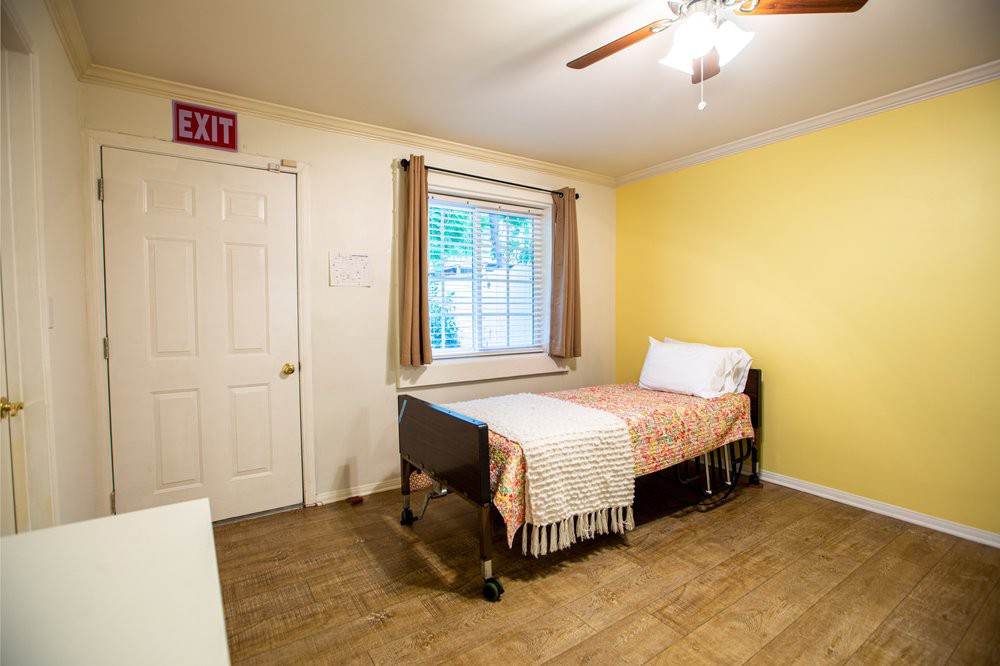 A simple bedroom with a single bed, wooden flooring, and a window with curtains.