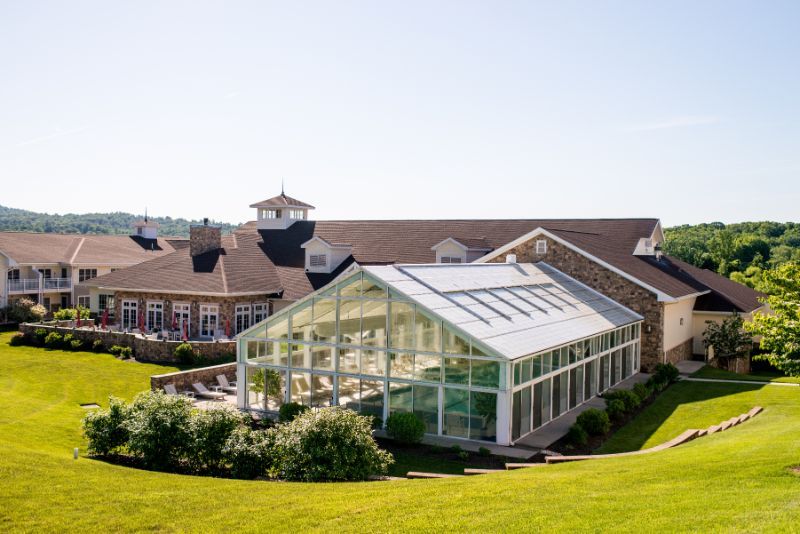 A modern greenhouse attached to a traditional building on a sunny day, surrounded by a well-kept lawn.