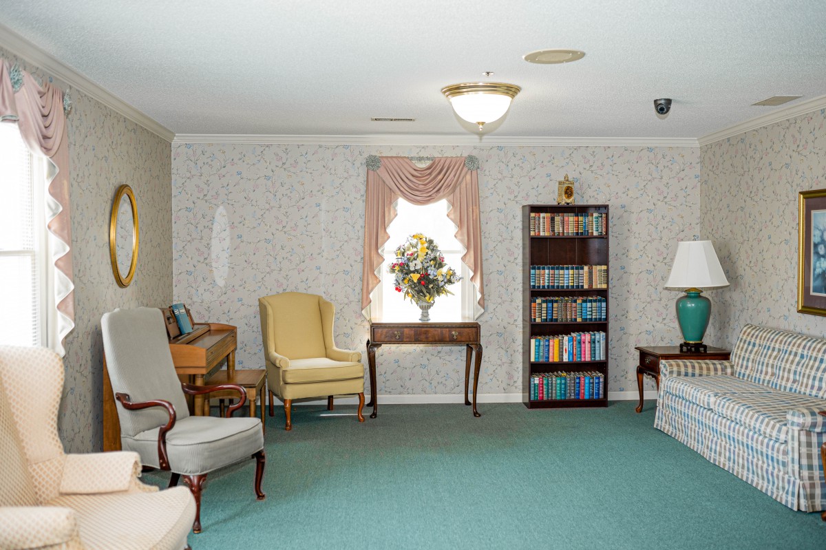 A cozy living room with armchairs, a bookshelf, and a window with drapes.