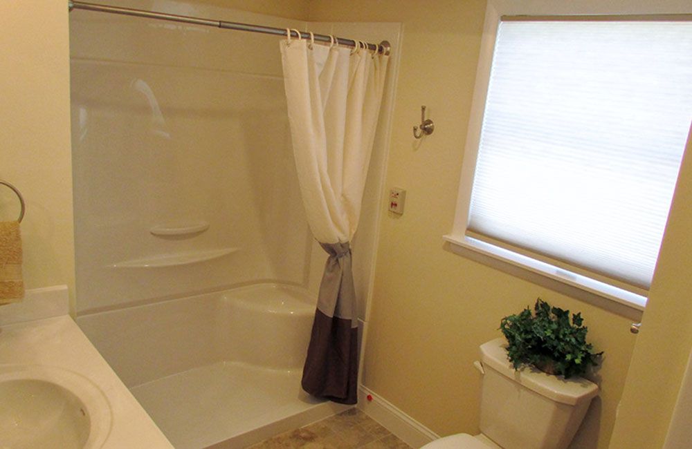 A bathroom with a shower, curtain, and toilet near a window.