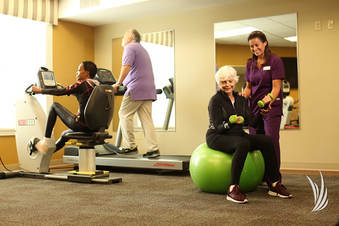 Seniors engaging in physical exercise at a gym, supported by a trainer.