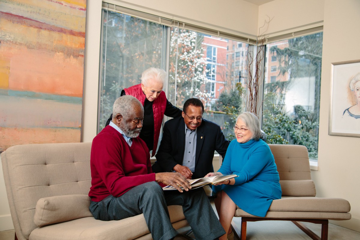 A group of seniors sitting together on a sofa, enjoying a photo album indoors.