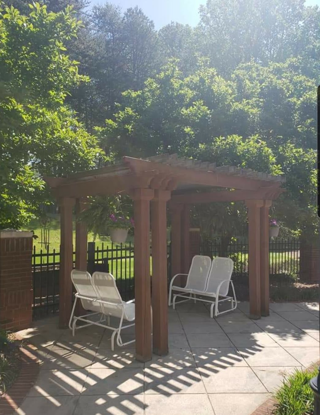 A wooden pergola providing shade over white outdoor chairs on a sunny patio.
