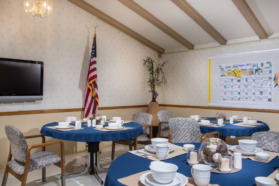 A dining area set up with tables featuring blue tablecloths, arranged with plates and cups, alongside an American flag displayed in the corner.