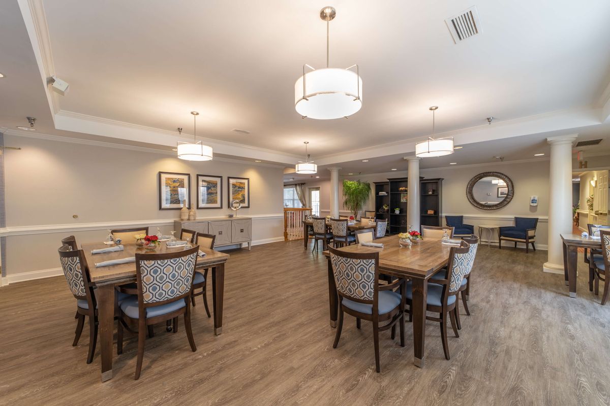 A modern dining area with neatly arranged tables and chairs, featuring elegant lighting and a wooden floor.