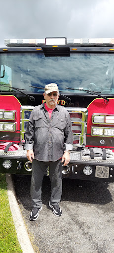 A firefighter stands in front of a fire truck, showcasing pride in his profession.