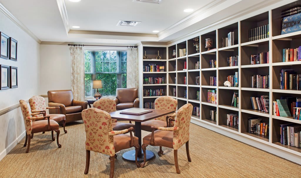 A cozy library room with bookshelves, a table, and armchairs by the window.