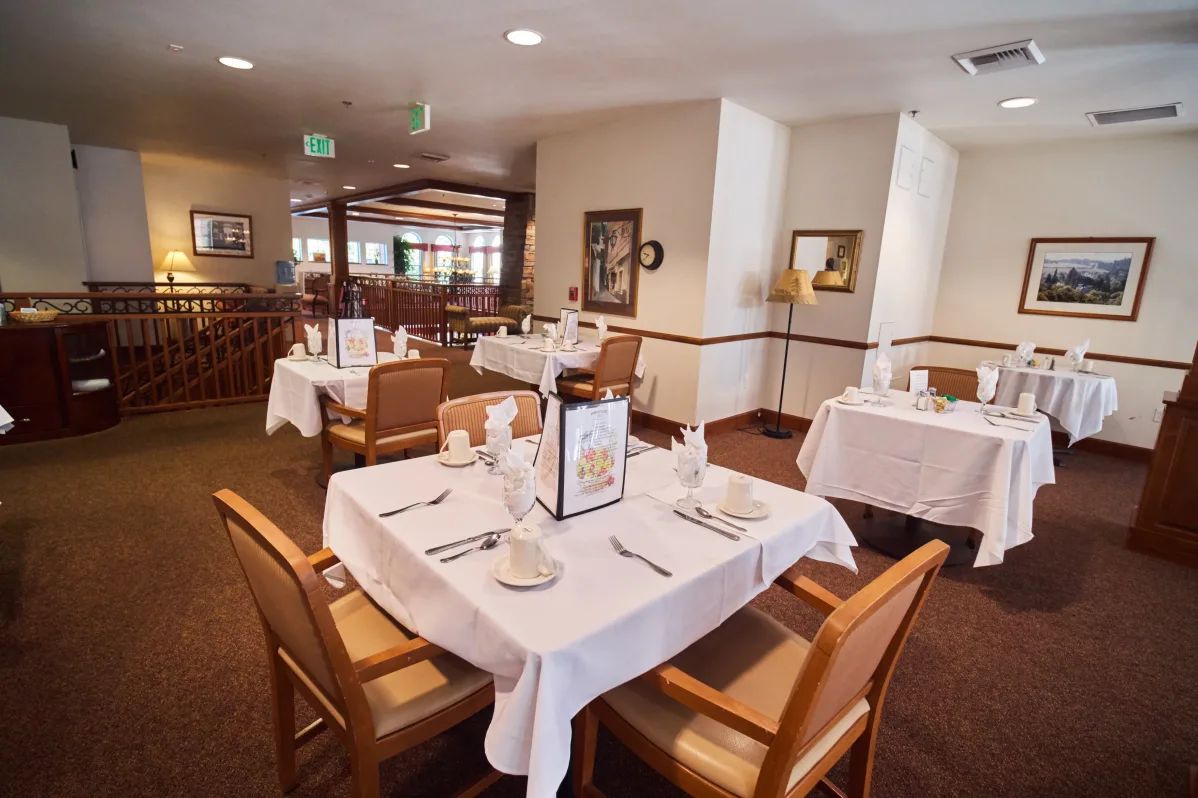 A well-arranged dining area with tables set with white tablecloths and neatly organized tableware.