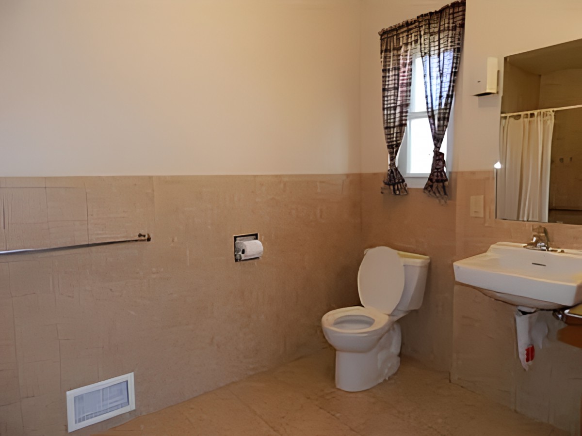 A clean and spacious bathroom with a toilet, sink, window with curtains, and beige tile flooring.