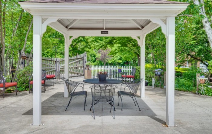 A charming outdoor gazebo with a metal table and chairs surrounded by lush greenery.