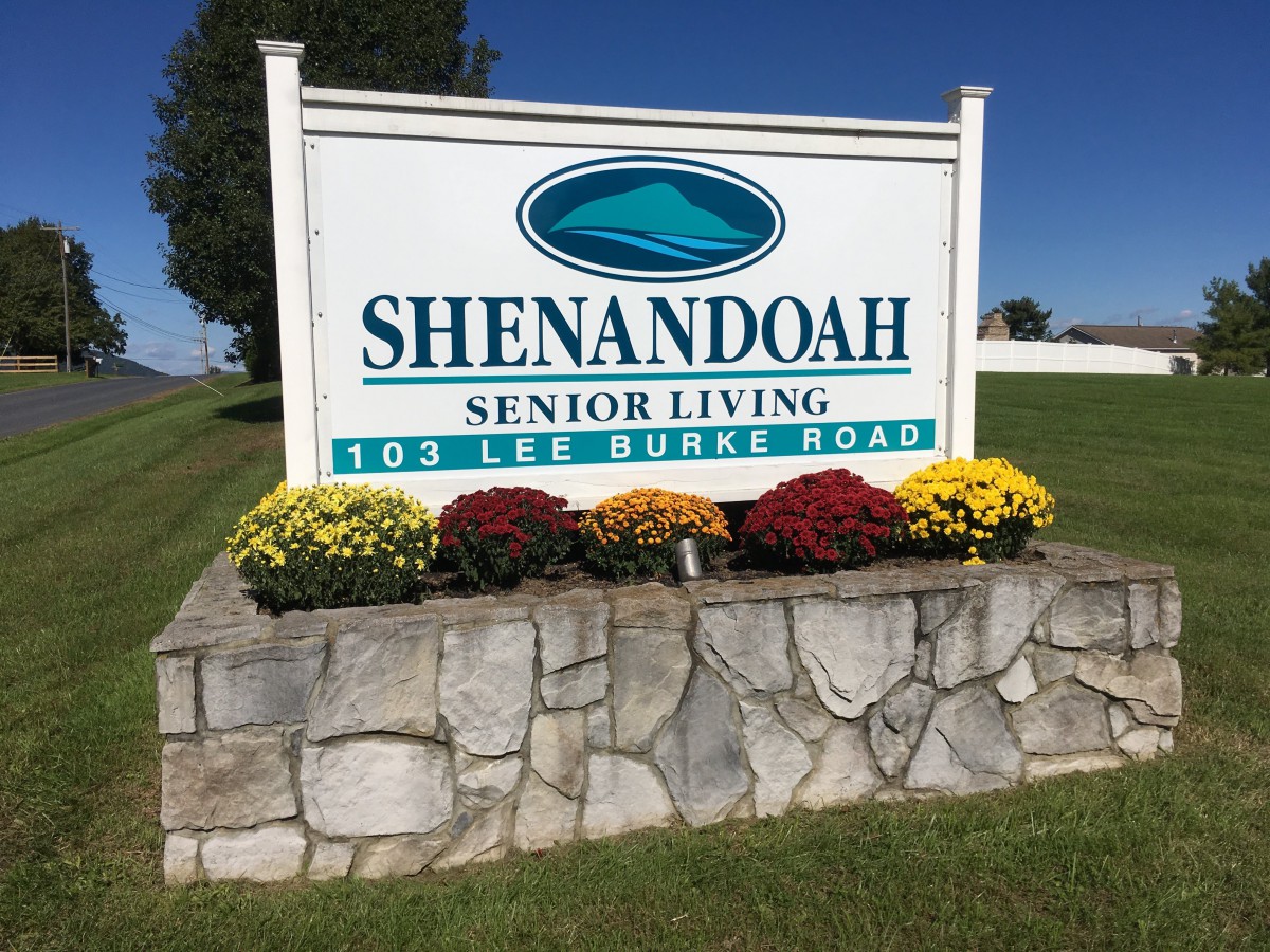Outdoor sign for Shenandoah Senior Living on Lee Burke Road, adorned with colorful flowers.