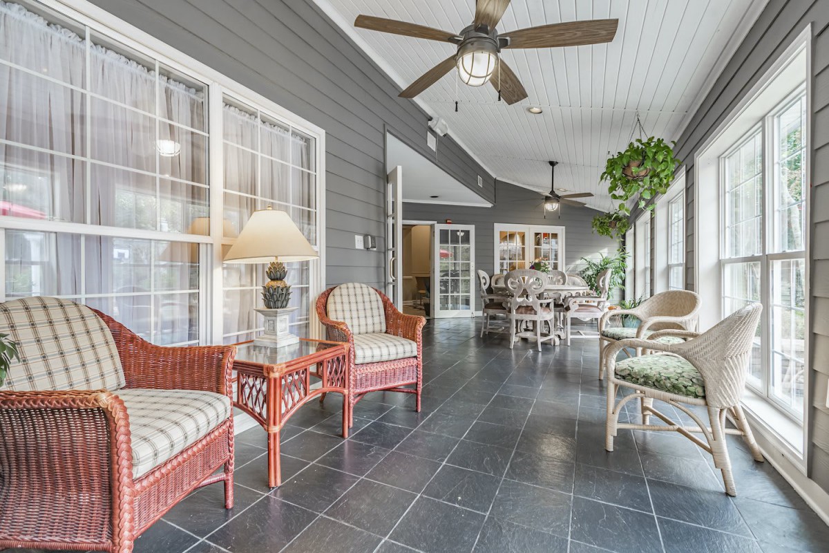 A bright sunroom featuring wicker furniture, large windows, and ceiling fans.