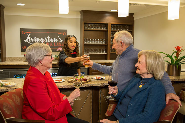 A group of elderly people enjoying wine and socializing at a bar, with a bartender serving drinks.