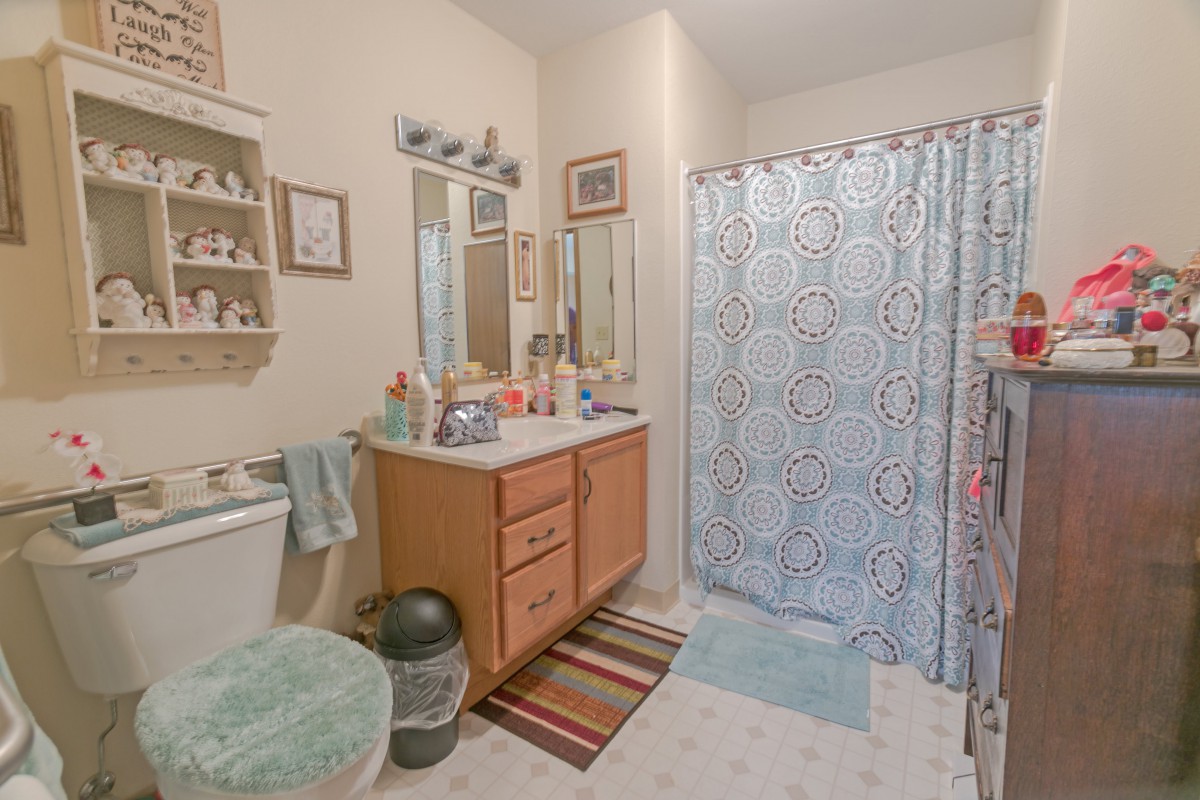 A bathroom featuring a vanity with a mirror, colorful shower curtain, and neatly organized items.
