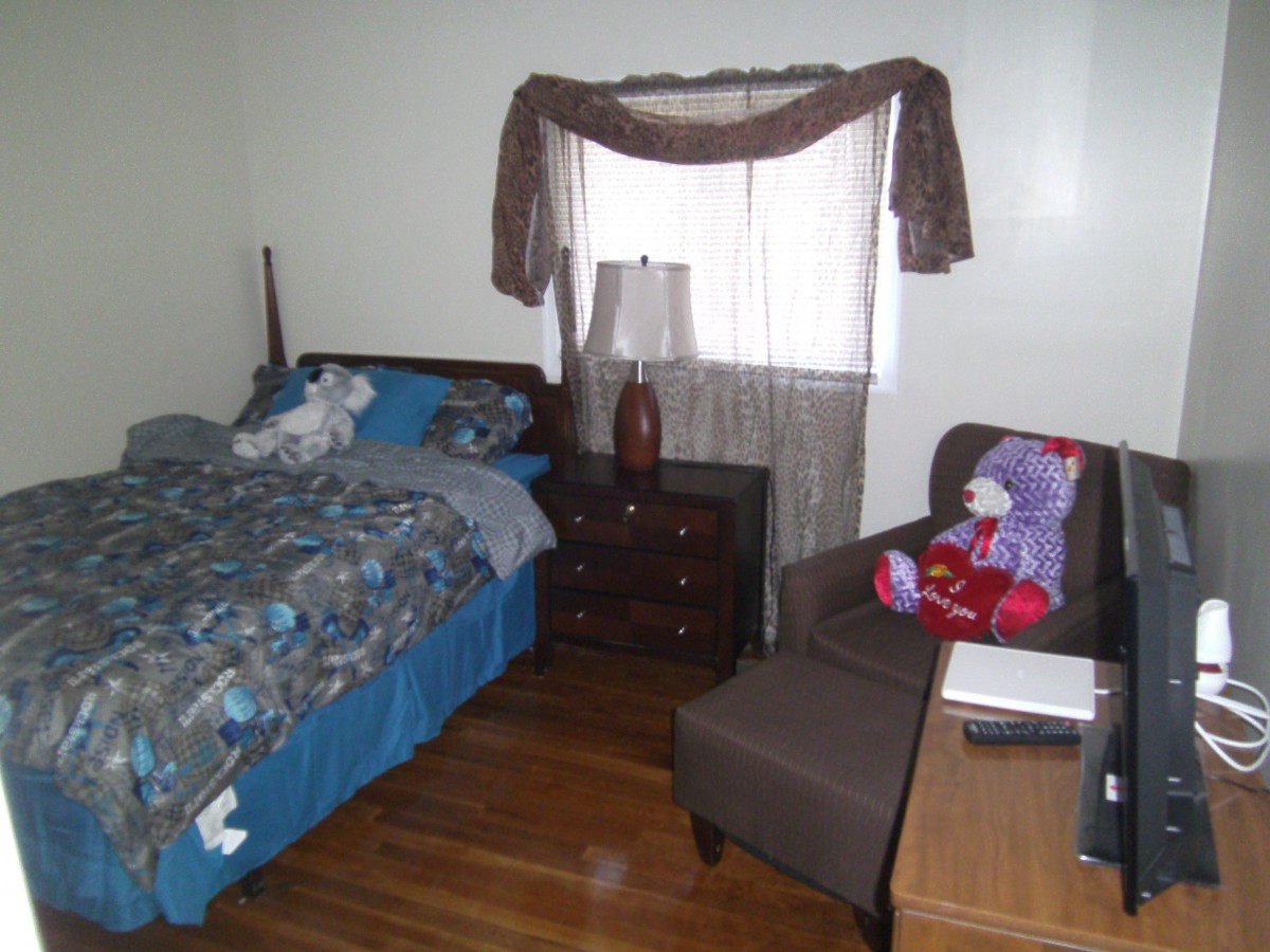 A cozy bedroom with a bed, chair, lamp, and window with curtains.