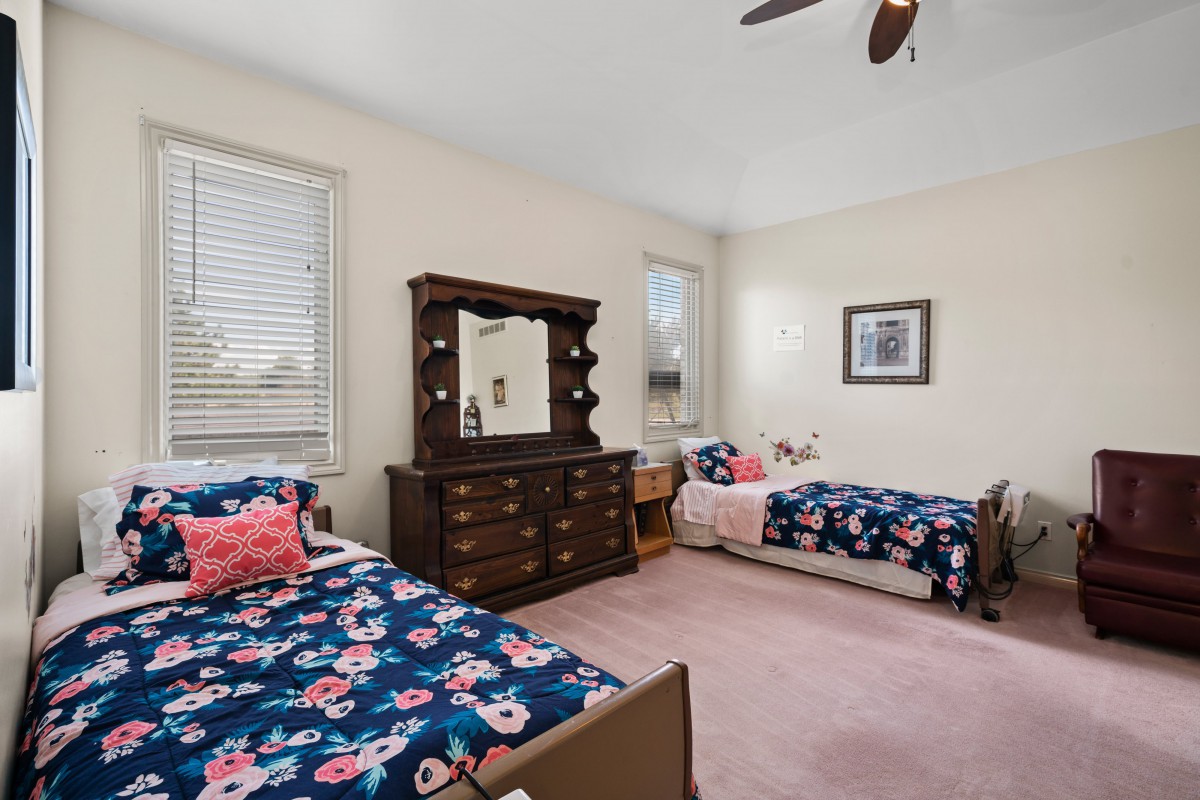 A cozy bedroom with twin beds featuring floral bedding and a wooden dresser with a mirror.