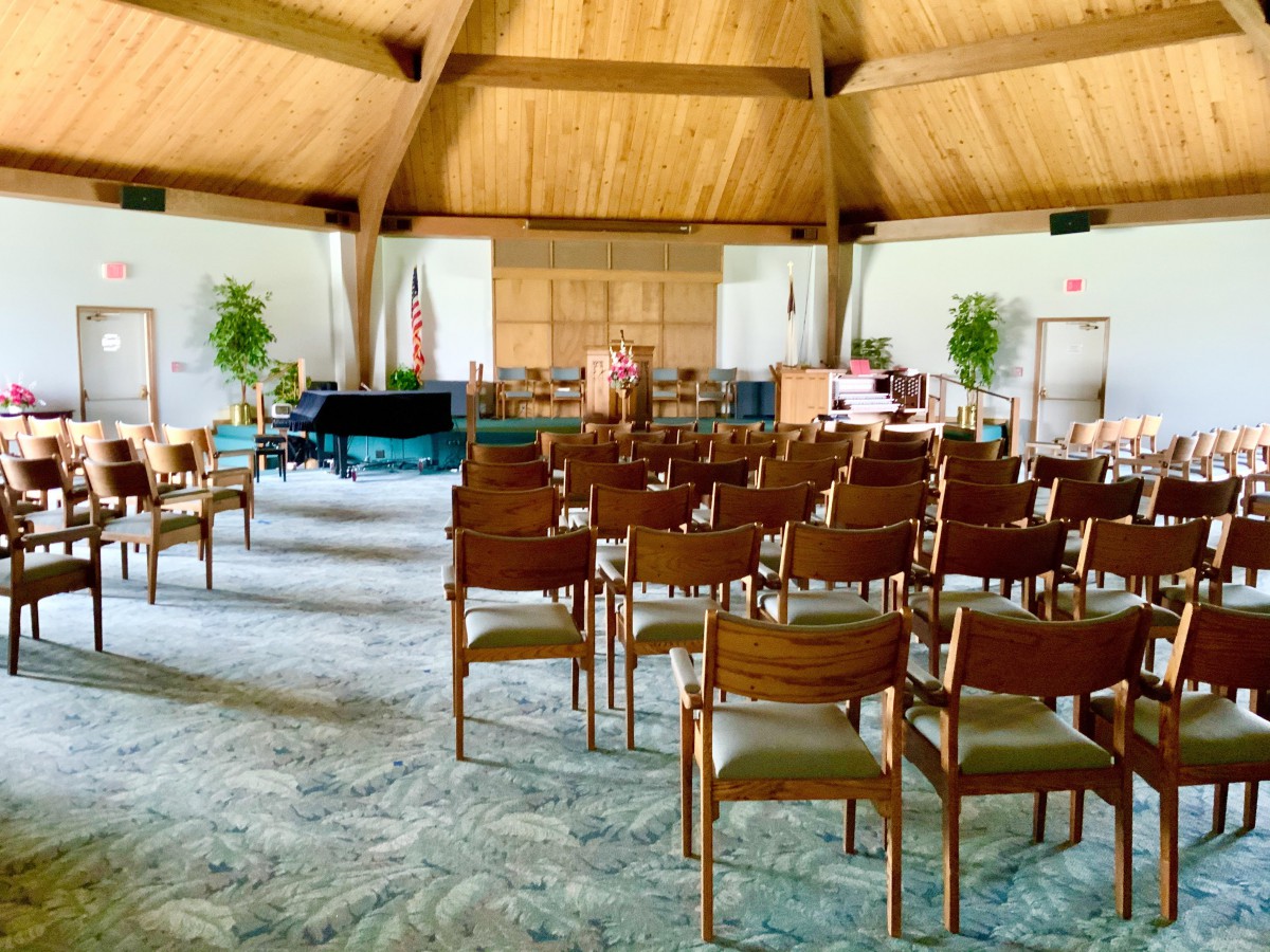 A church interior with wooden chairs arranged in rows, a piano, and a distinctive wooden ceiling.